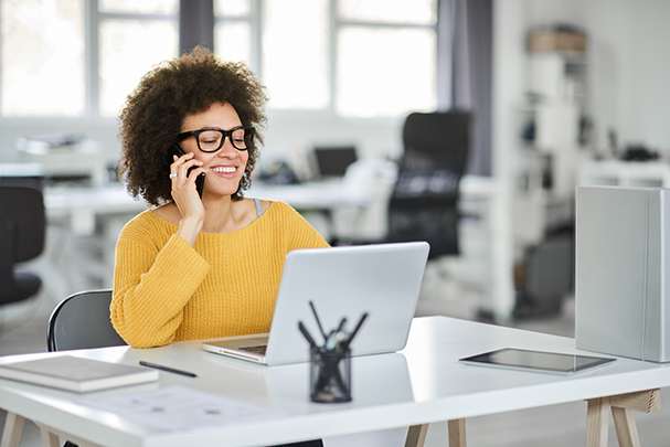 Charming mixed race woman talking on the phone and using a laptop to create eye-catching graphics.