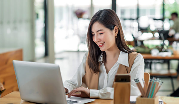 Happy young businesswoman sitting at table in cafe with tabletop computer.