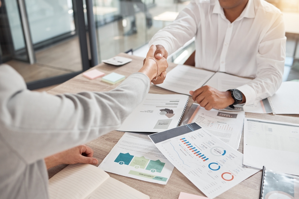 Two people shaking hands over desk.