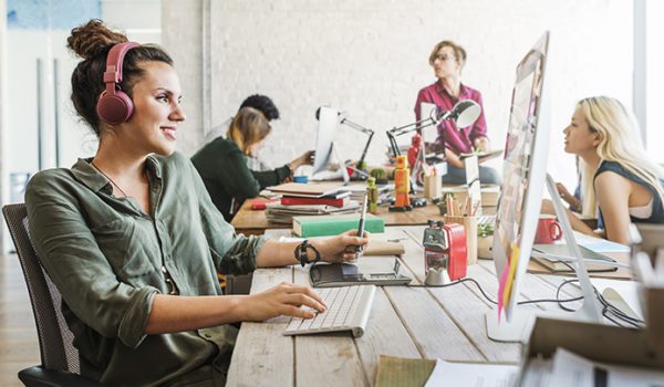 woman working on computer with headphones on among other coworkers