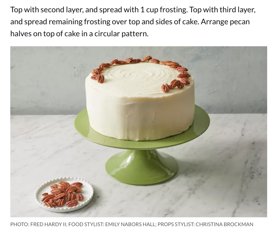 decorated hummingbird cake on cake stand with small bowl of pecans next to it 